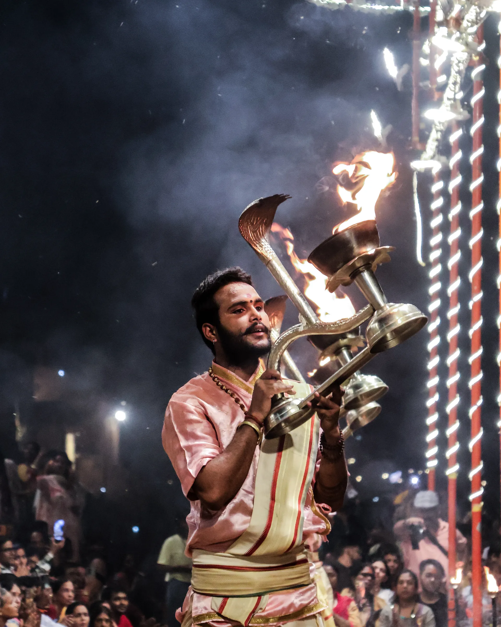 Priest holding a cobra-shaped brass lamp with flame during aarti
