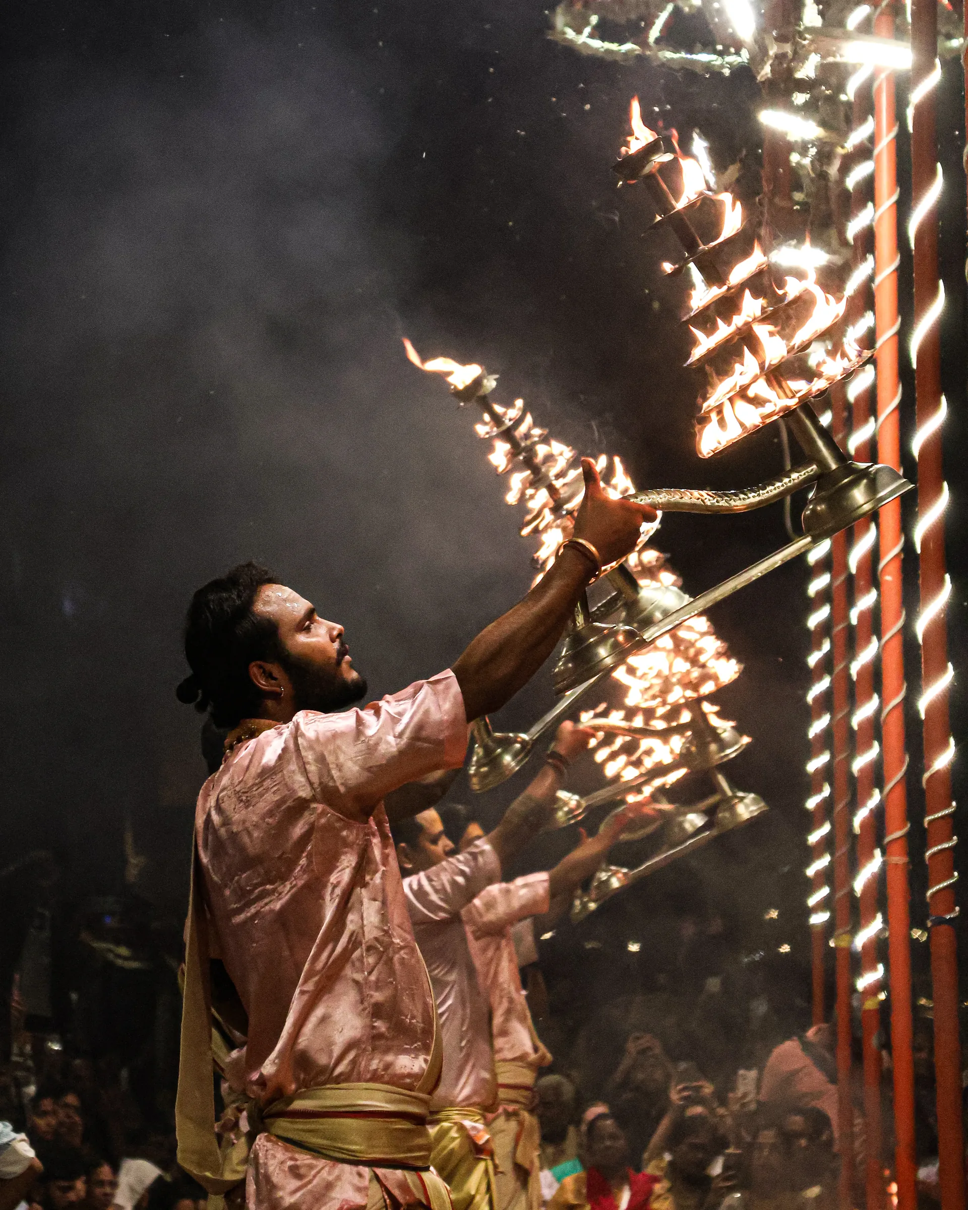 Priest lifting a lit multi-tier lamp during Ganga Aarti ceremony