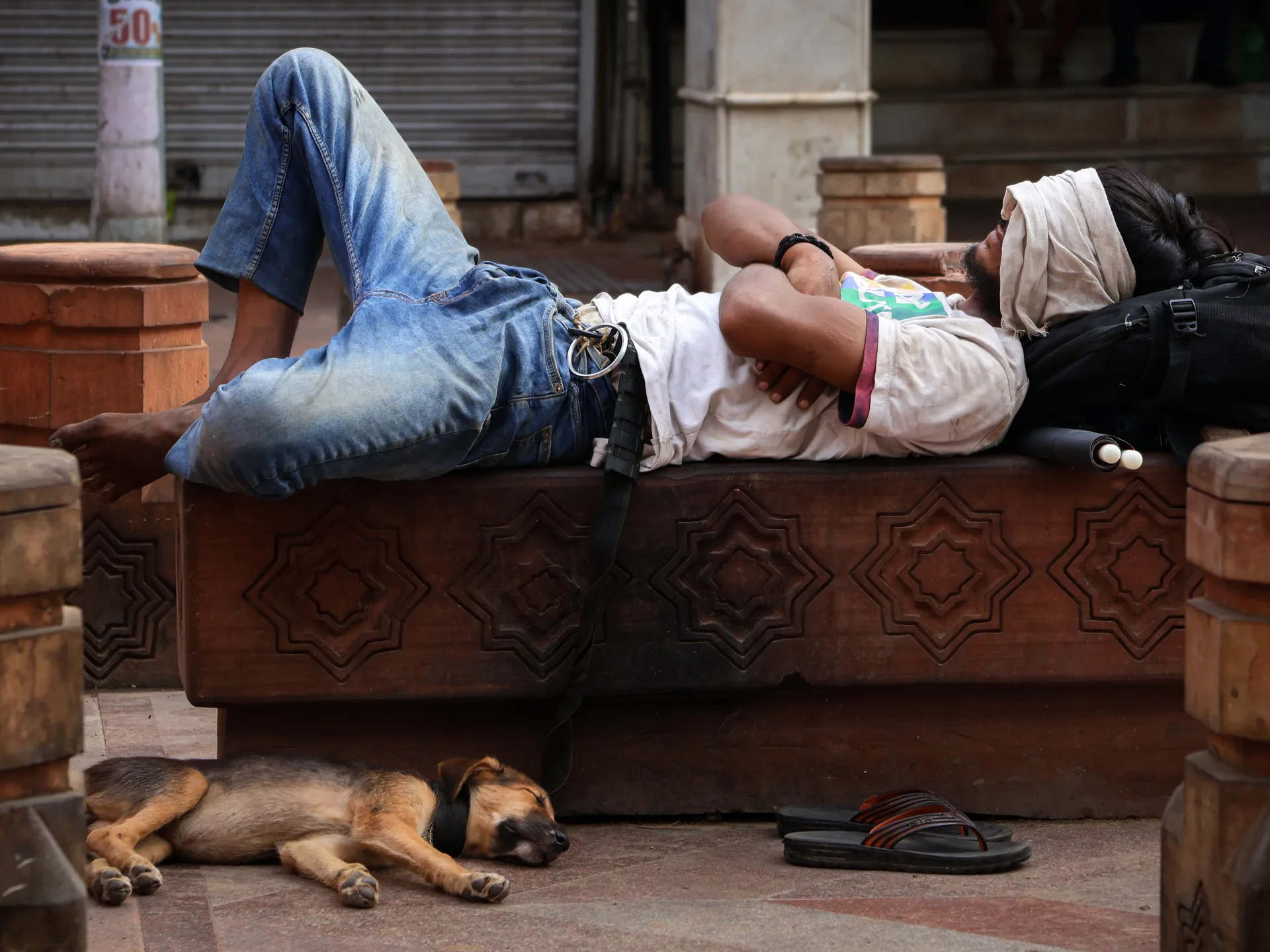 Man resting on a carved stone bench beside a sleeping street dog